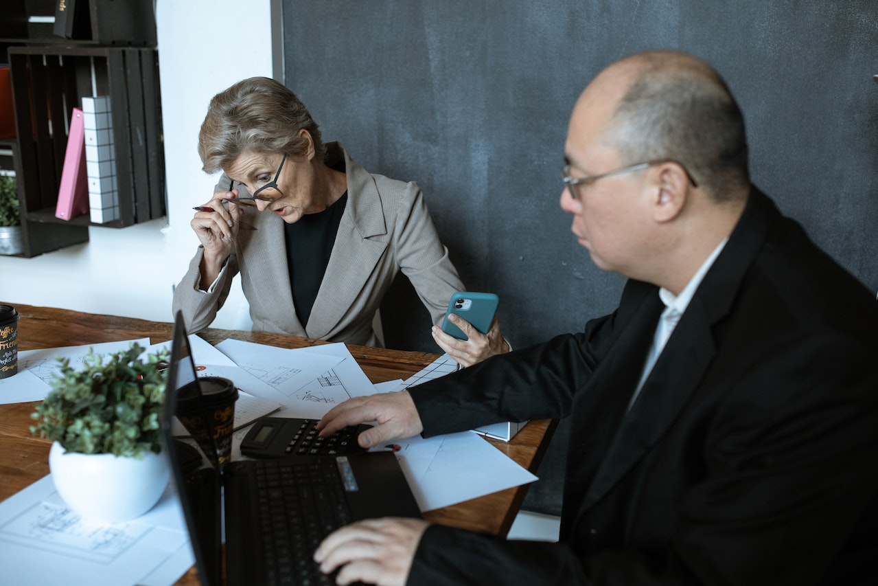 Takeoff Monkey blog article, The Future of the Construction Estimating Industry image: two colleagues sitting, talking at a table with scattered papers and a laptop